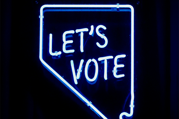Ein blaues Leuchtschild vor schwarzen Hintergrund mit der Aufschrift "Let's vote".