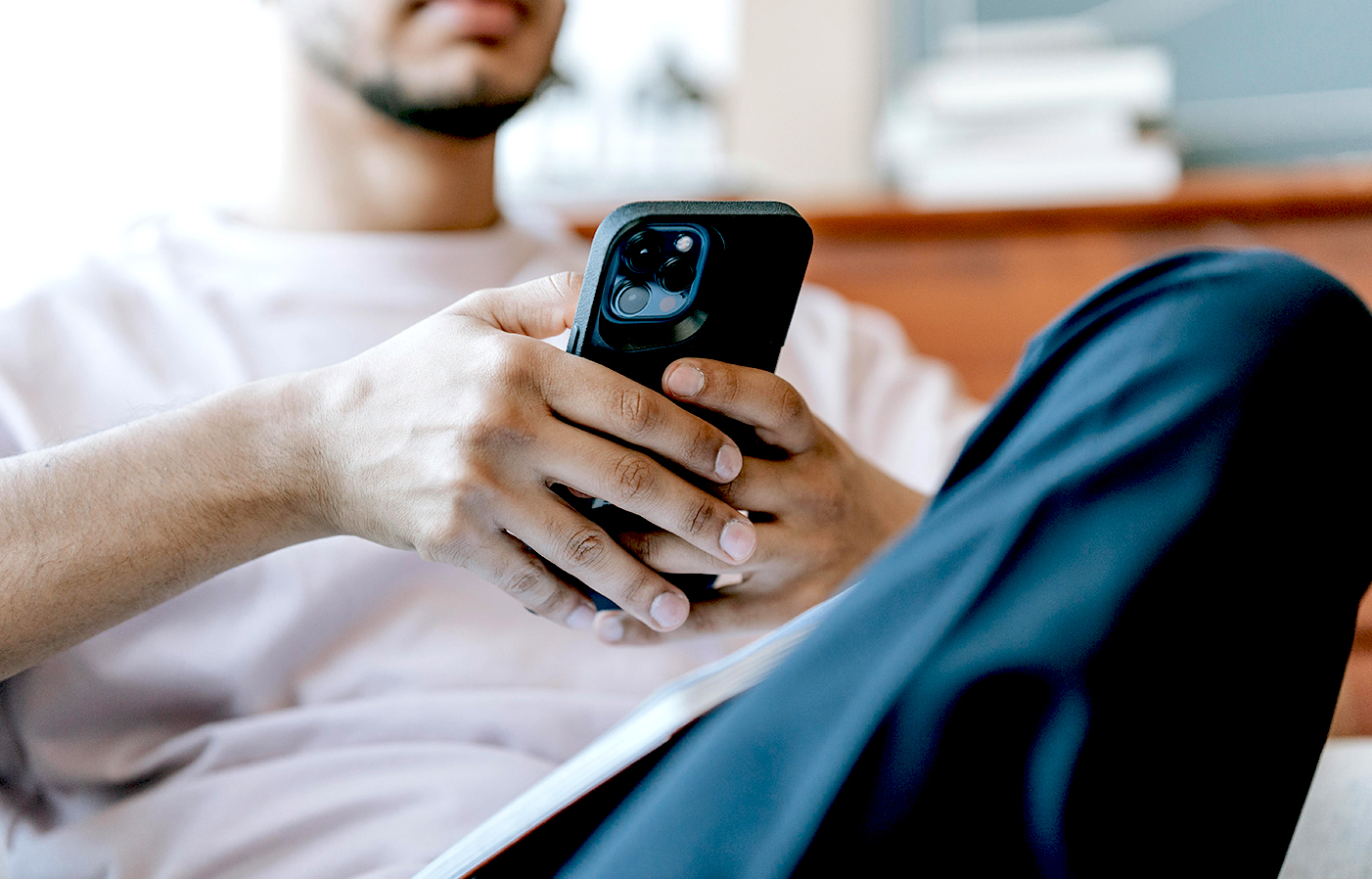 Junger Mann hält ein Smartphone. Das Smartphone steht im Bildmittelpunkt. Der Mann ist unscharf im Hintergrund zu sehen.