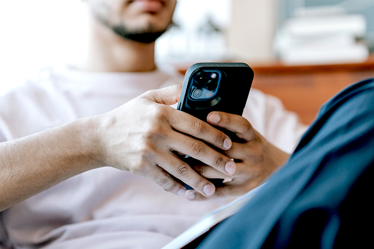 Junger Mann hält ein Smartphone. Das Smartphone steht im Bildmittelpunkt. Der Mann ist unscharf im Hintergrund zu sehen.