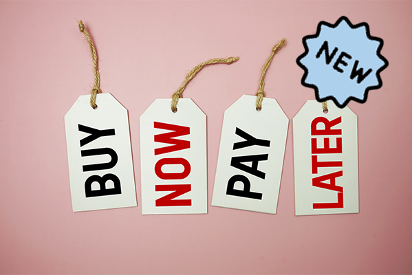 Vier Etiketten mit der Aufschrift "Buy now pay later" vor einem pinken Hintegrund. Jedes Wort ist einzeln auf einem Etikett.