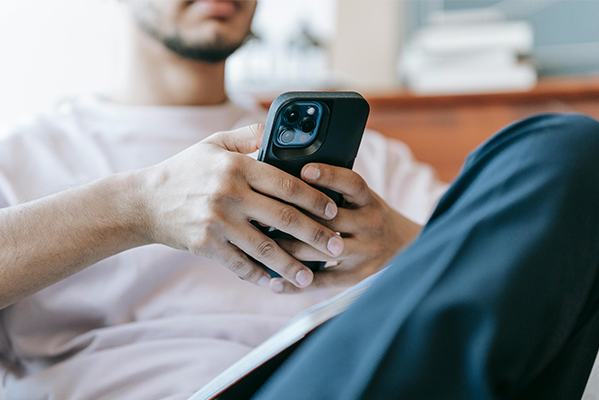Ein junger Mann mit einem Handy auf der Couch beim surfen.