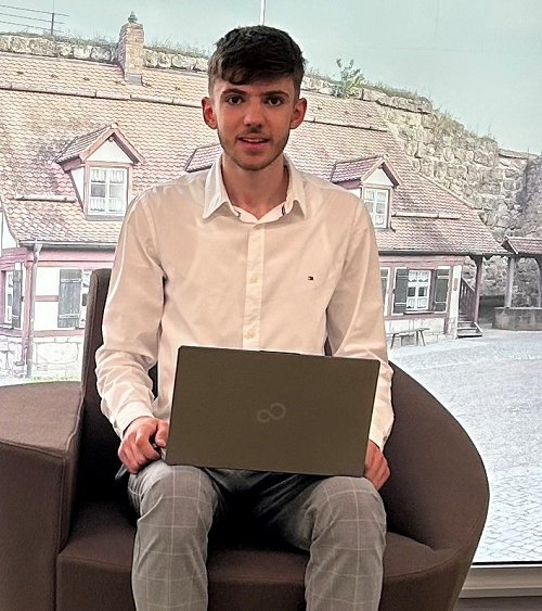 Auszubildender Arbijon Hasani in seinem Ausbildungsbetrieb mit einem Laptop auf dem Schoß