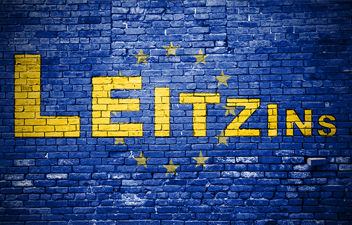 Der Begriff "Leitzins" in gelber Schrift auf einer blauen Backsteinwand. Rundherum die Sterne der Europaflagge.